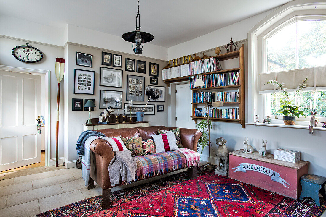 Shelving and prints above leather sofa at window in living room of Stamford home Lincolnshire England UK