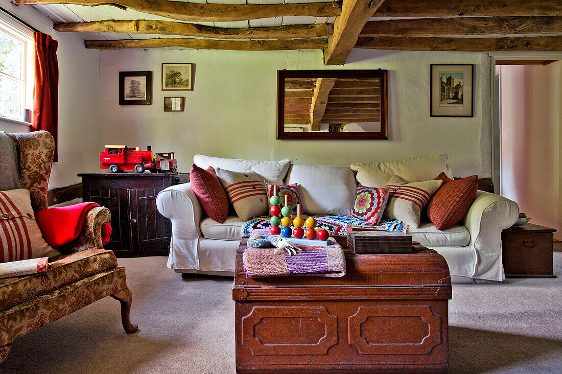 Kinderspielzeug auf einer Reisetruhe mit weißem Sofa im mit Balken versehenen Wohnzimmer eines Hauses in Cambridge, England, UK