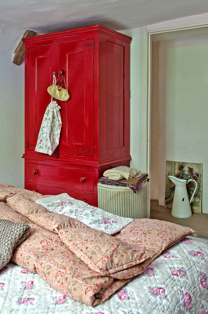 Rot bemalter Kleiderschrank im Schlafzimmer mit geblümten Steppdecken in einem Cottage in Cambridge, England, UK