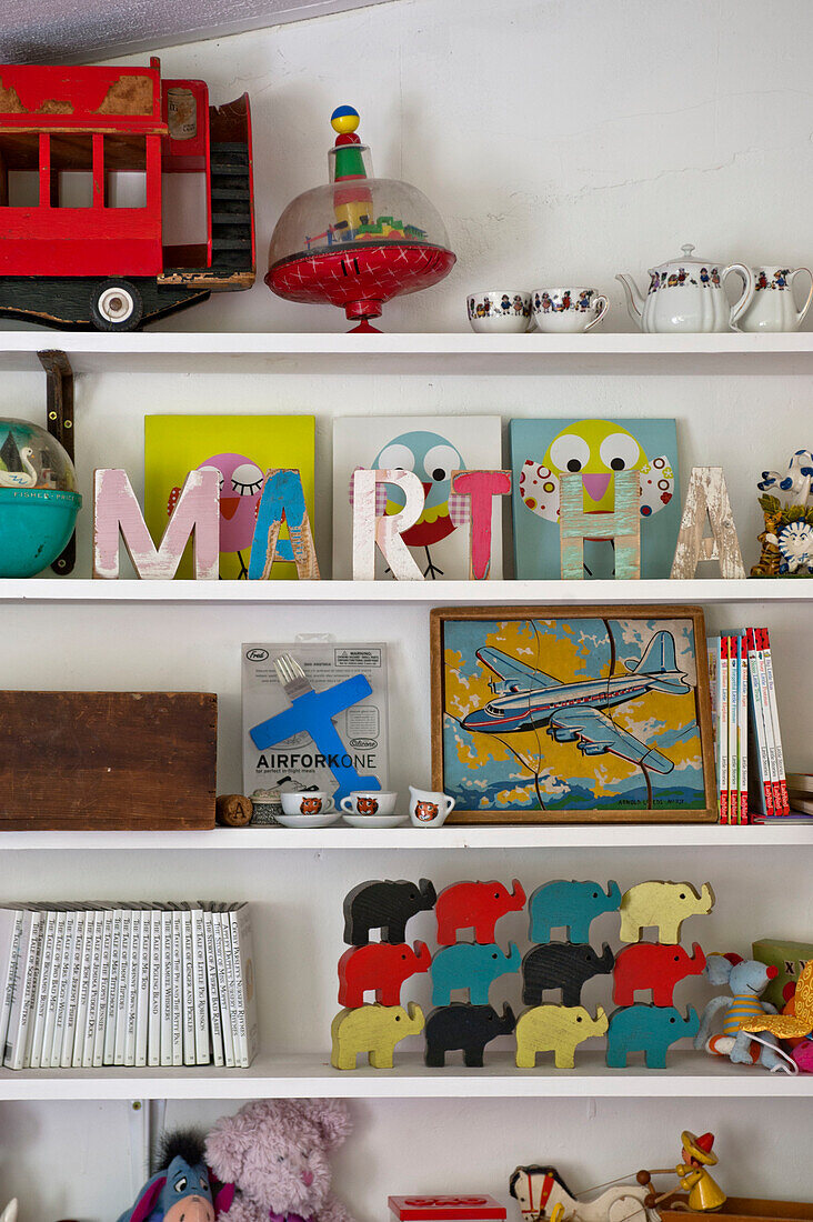 Toys and artwork with name 'MARTHA' on shelves in girls room of Cambridge cottage England UK
