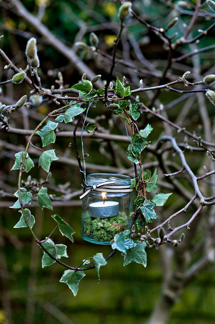 Lit tealight in jam-jar with moss and natural wreath of ivy in London garden England UK