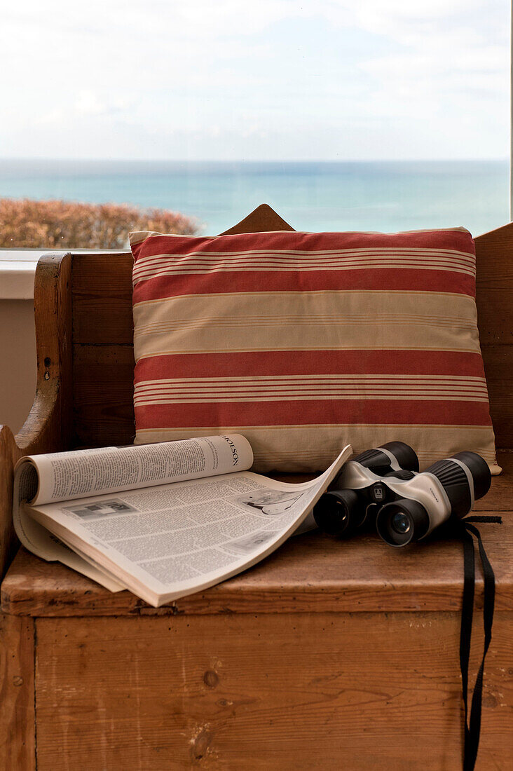 Striped cushion and binoculars on wooden bench seat in window of beach house Cornwall England UK