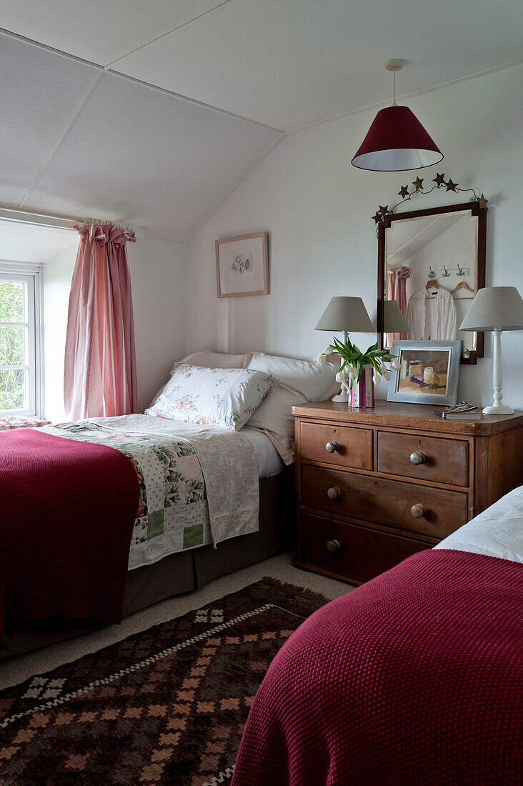 Zwillingsbetten mit weinroten Bezügen und einer hölzernen Kommode in einem Strandhaus in Cornwall England UK