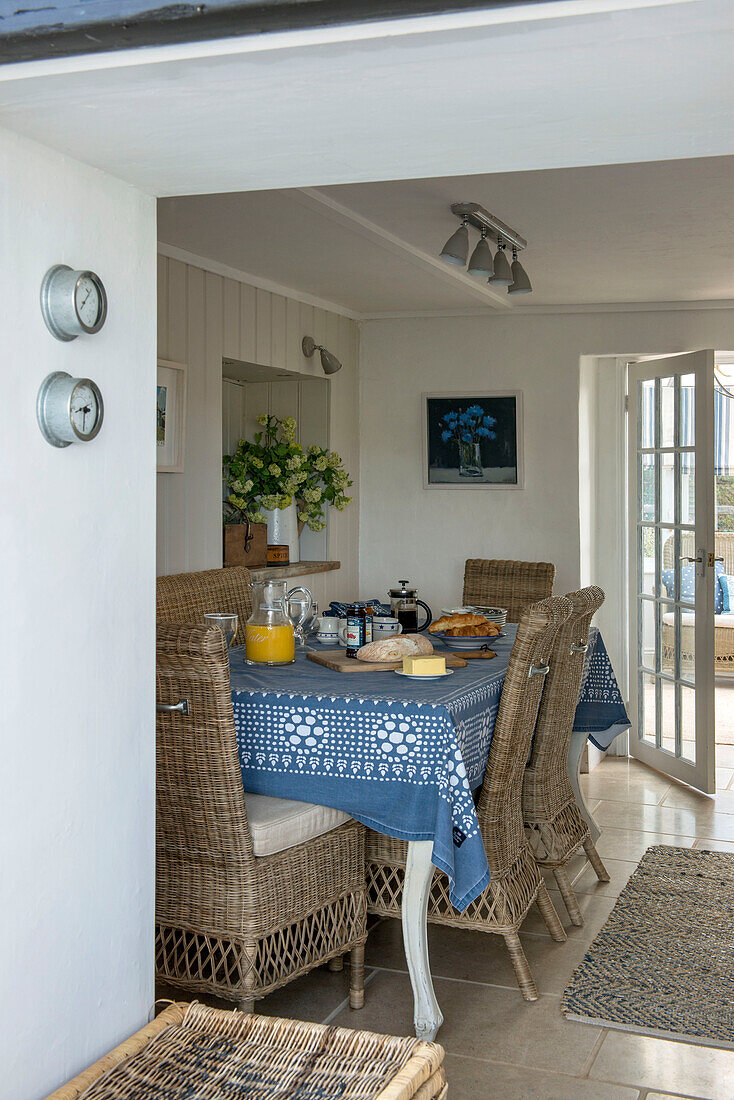 Breakfast table with blue tablecloth and wicker chairs in Penzance farmhouse kitchen Cornwall England UK