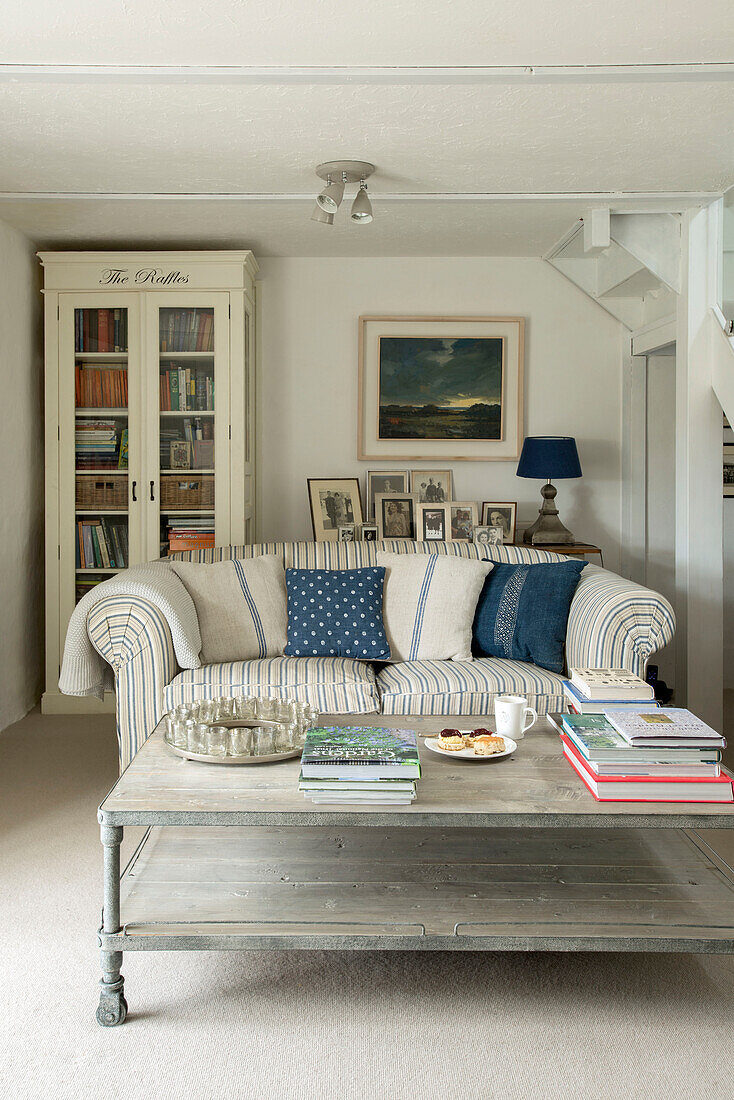 Familienfotos mit Bücherregal mit Glasfront und Sofa im Wohnzimmer eines Bauernhauses in Penzance, Cornwall, England UK