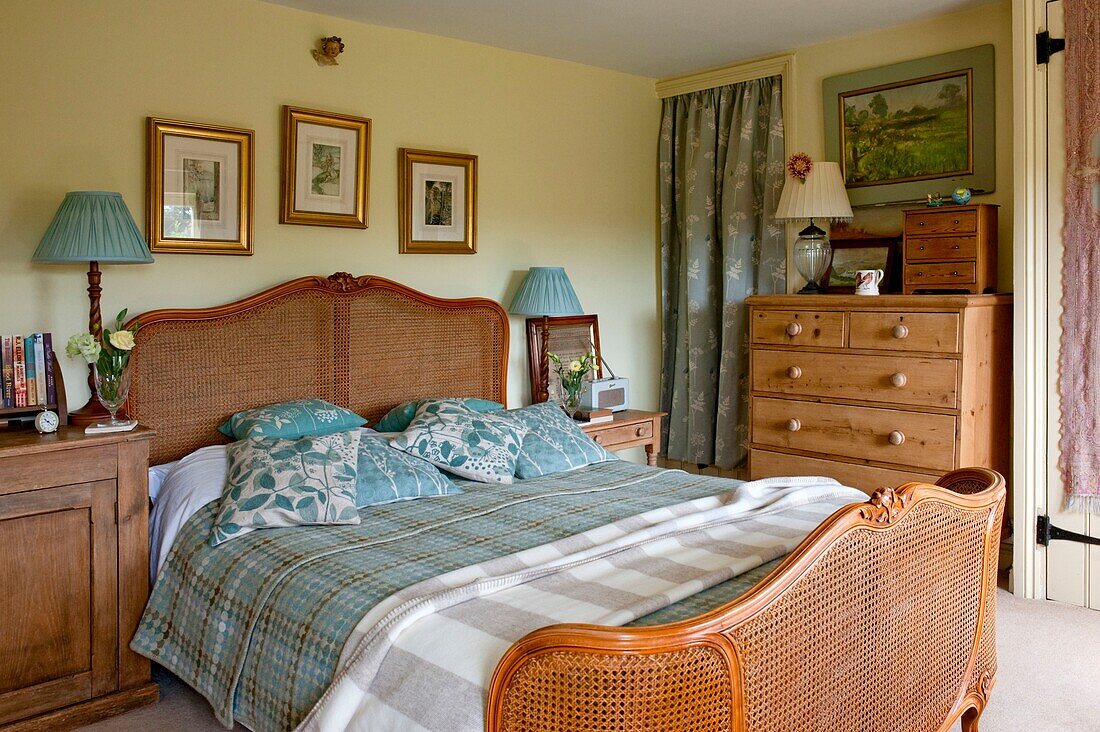 Wicker bed with gilt-framed artwork and leaf patterned cushions in Edworth bedroom Bedfordshire England UK