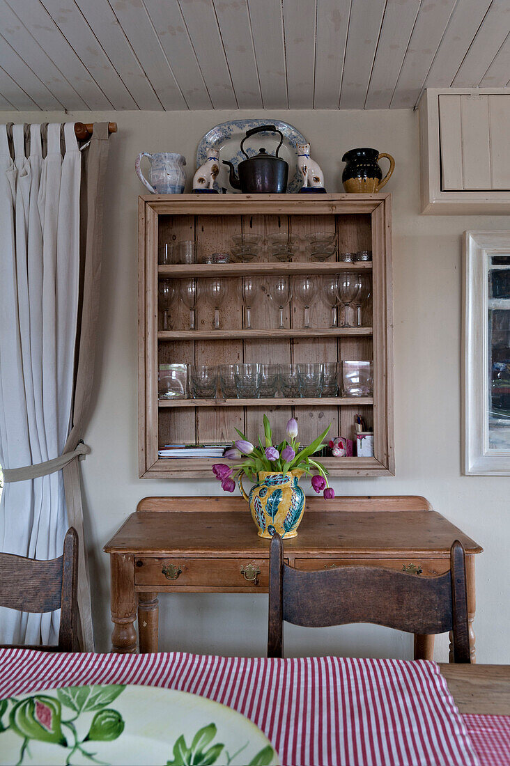 Weingläser im Schrank über geschnittenen Tulpen auf hölzernem Beistelltisch in Strandhaus in Cornwall England UK