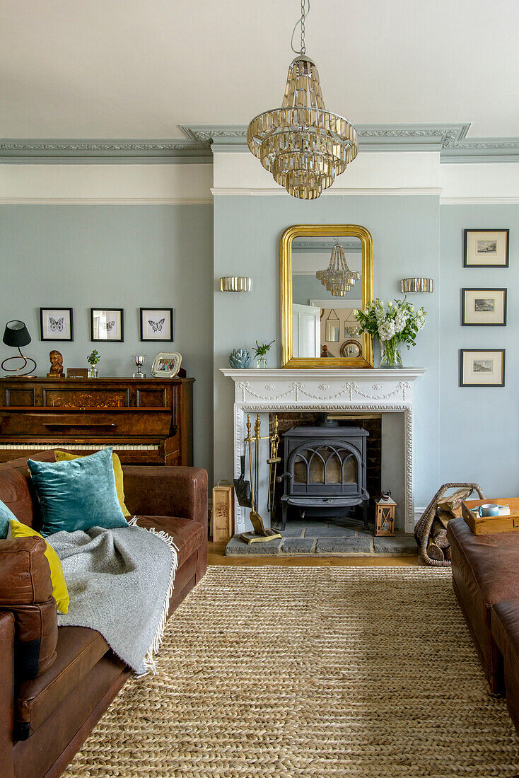 Brown leather sofa in light blue living room with glass chandelier and woodburning stove in Tunbridge Wells family home Kent England UK