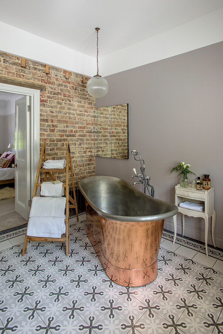 Copper bath with tiled floor and exposed brick wall in bathroom of Tunbridge Wells home Kent England UK