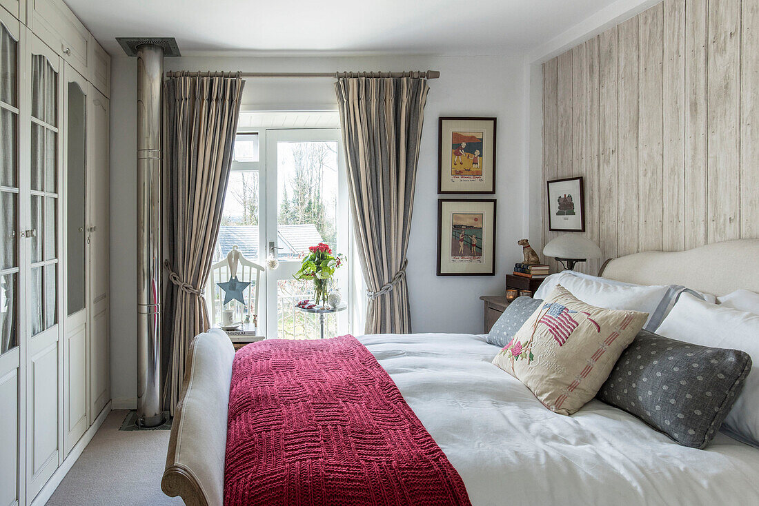 Schnittblumen im Fenster eines Schlafzimmers mit roter Decke und gerahmten Kunstwerken in einem Bauernhaus in Penzance, Cornwall, Großbritannien