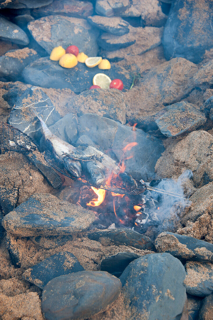 Fisch und Tomaten mit Zitronen auf einem Lagerfeuer aus Stein Cornwall UK