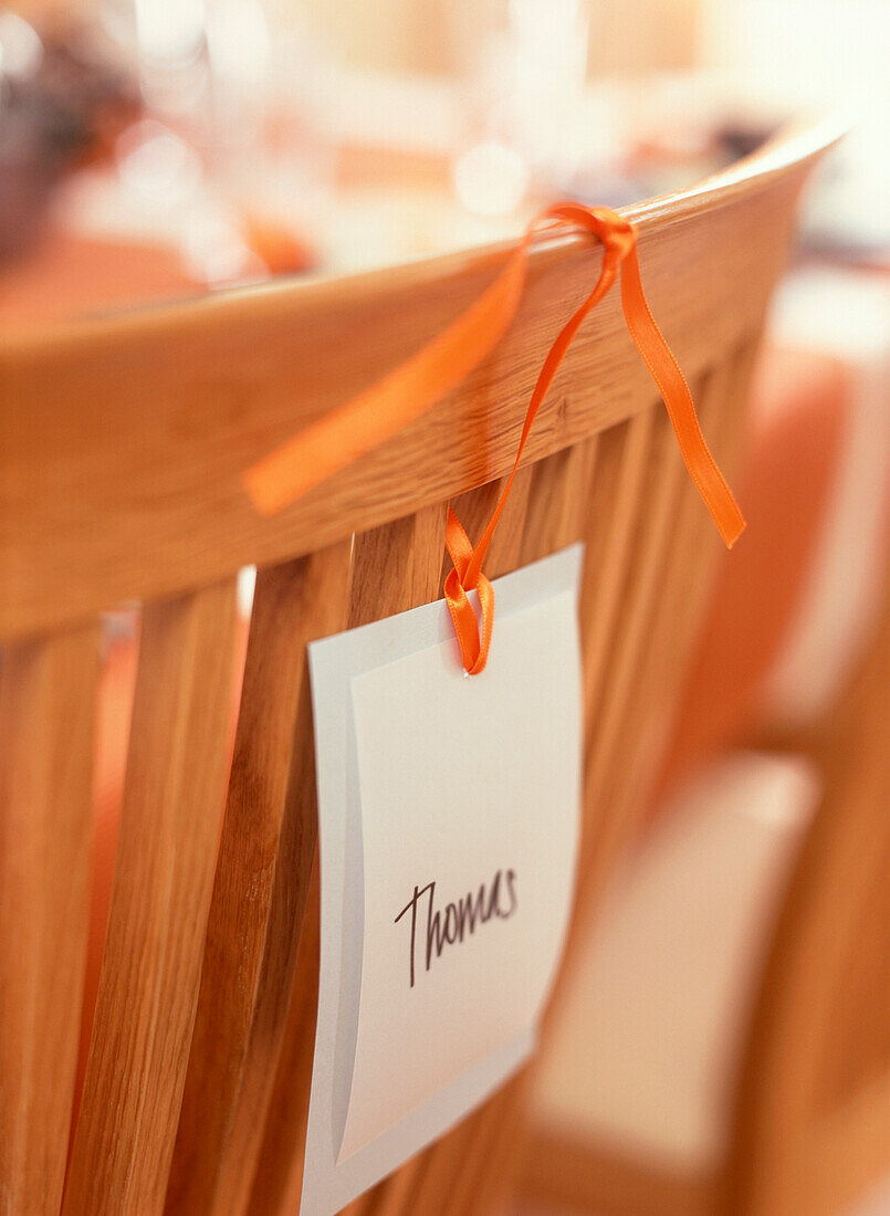Namensschild mit Thomas, das mit einem orangefarbenen Band an die Rückenlehne eines Esszimmerstuhls gebunden ist