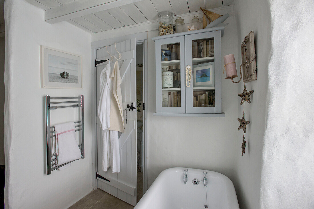 Glass fronted cabinet above freestanding bath with towel rail in Marazion beach house Cornwall UK