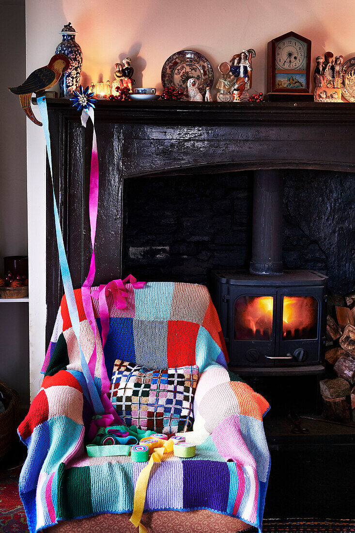 Christmas streamers on mantelpiece above armchair with knitted blanket at lit fireside Shropshire cottage England UK