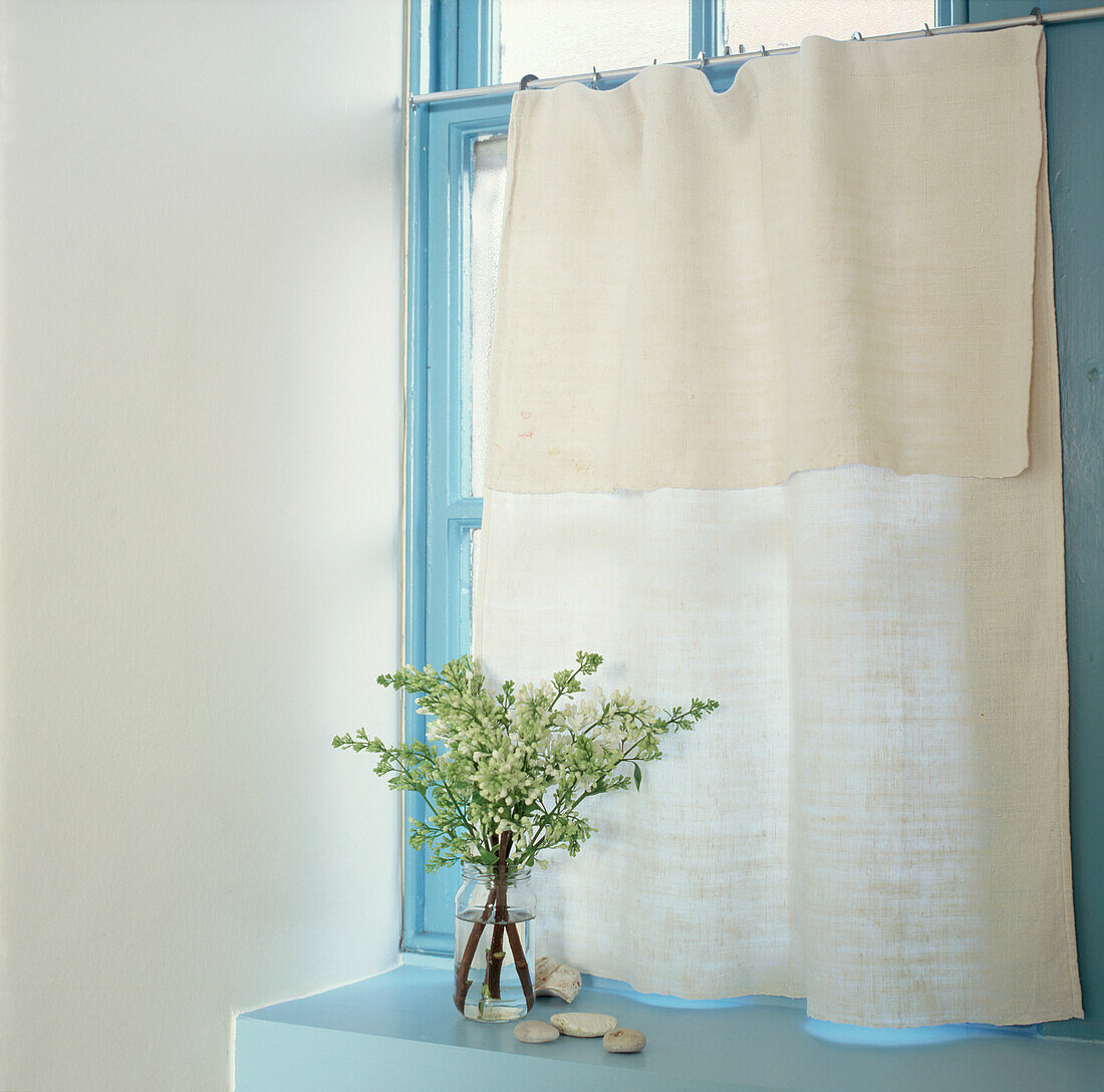 Stilleben mit weißen Blumen vor einem Leinenvorhang und einem bunten, blau bemalten Fensterrahmen