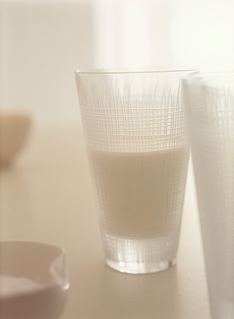 Glasses of fresh milk in etched tumblers on white kitchen table