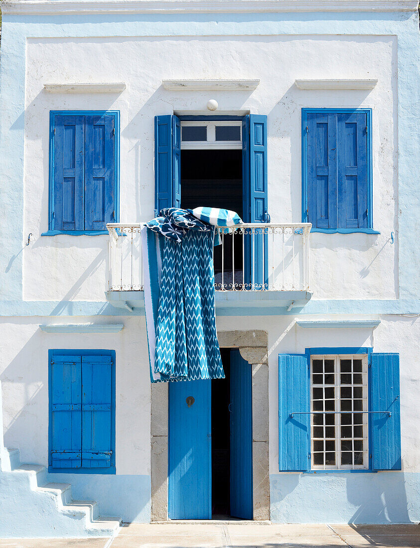 Airing bedding on balcony of Greek villa with blue painted shutters