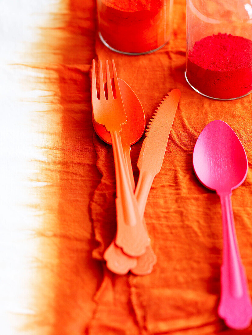 Oranges Besteck mit rosafarbenem Löffel auf bandgefärbtem Stoff mit Puder