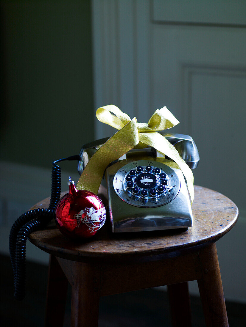 Red bauble and rotary dial phone tied with ribbon on wooden stool