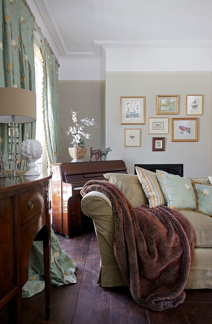 Fur throw on sofa and polished wood sideboard and harpsichord in Cranbrook home, Kent, England, UK