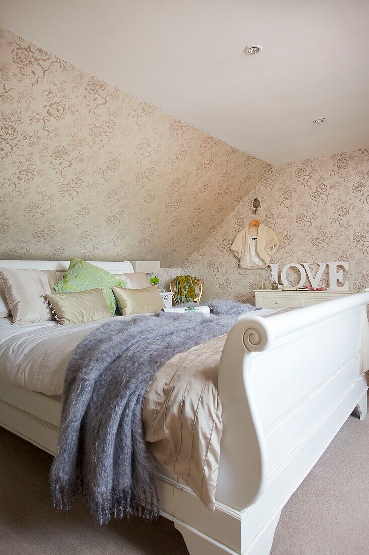 Painted white bed with blue blanket and floral wallpaper in bedroom of Cranbrook home, Kent, England, UK