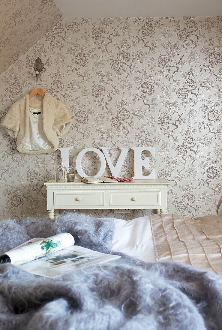 Patterned wall paper and wool throw with single word 'love' in bedroom of Cranbrook home, Kent, England, UK