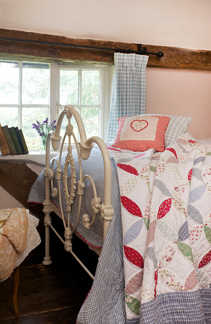 Metal worked footboard on single bed with patchwork quilt in Sandhurst cottage, Kent, England, UK