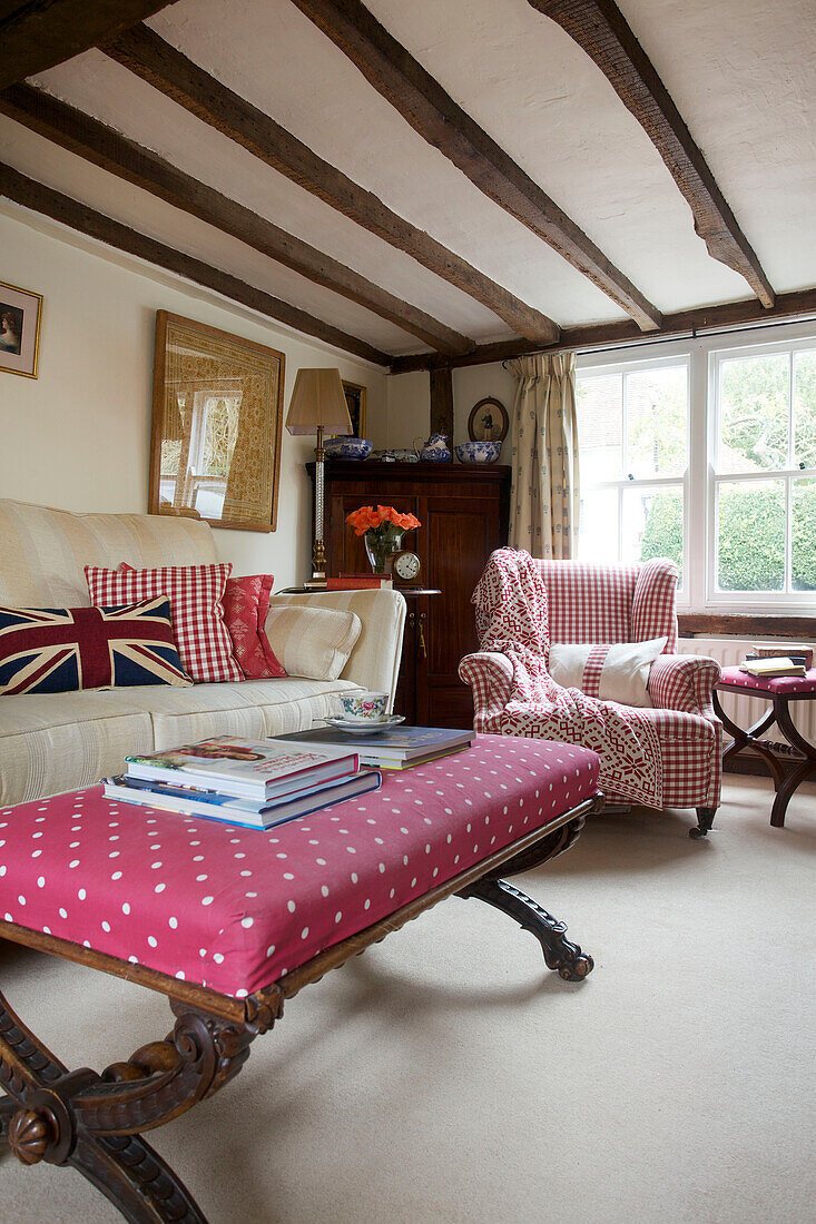 Books on re-upholstered antique footstool in timber framed living room of Egerton cottage, Kent, England, UK