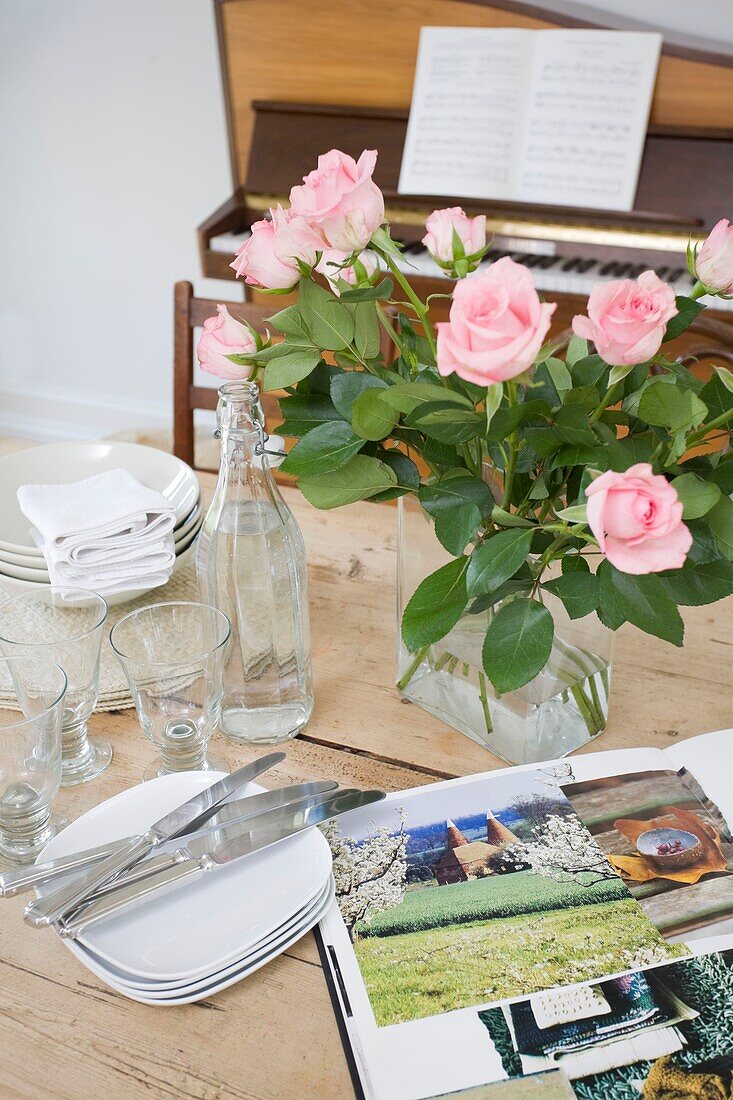 Cut roses and glassware on tabletop with sourcebook and piano in Tenterden family home, Kent, England, UK