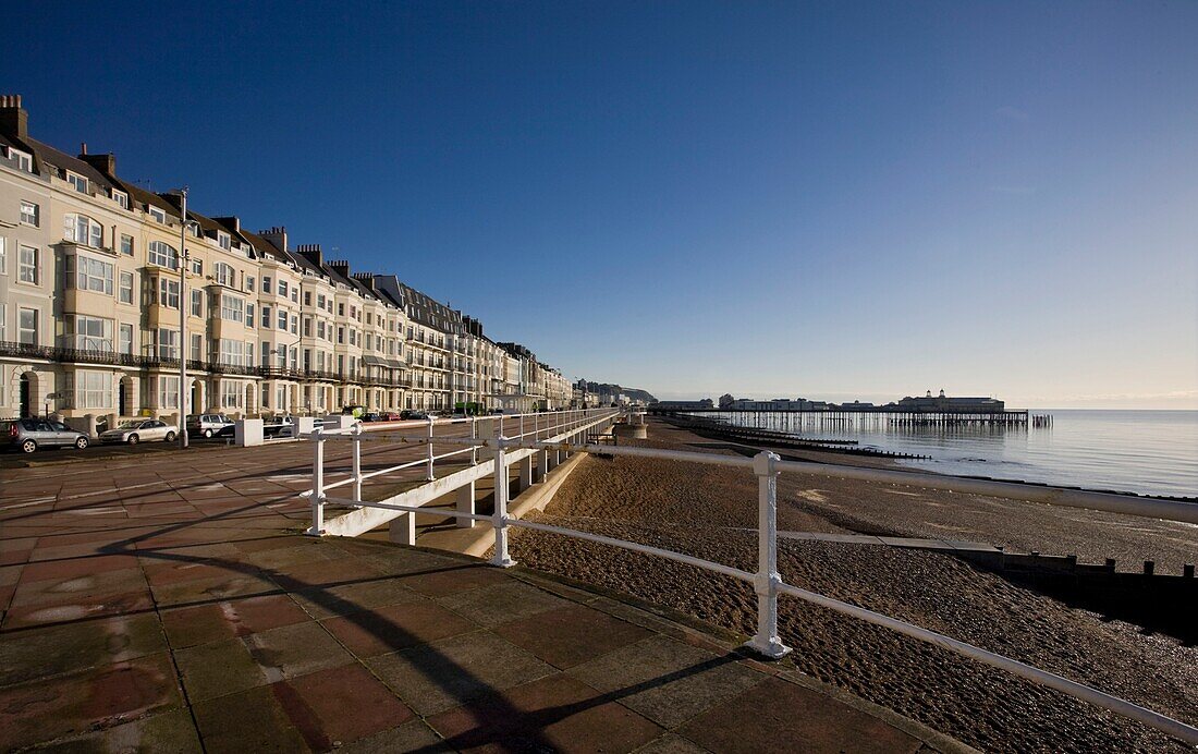 Seafront houses and promenade with shingle beach and distant pier in St Leonards on Sea, East Sussex, England, UK