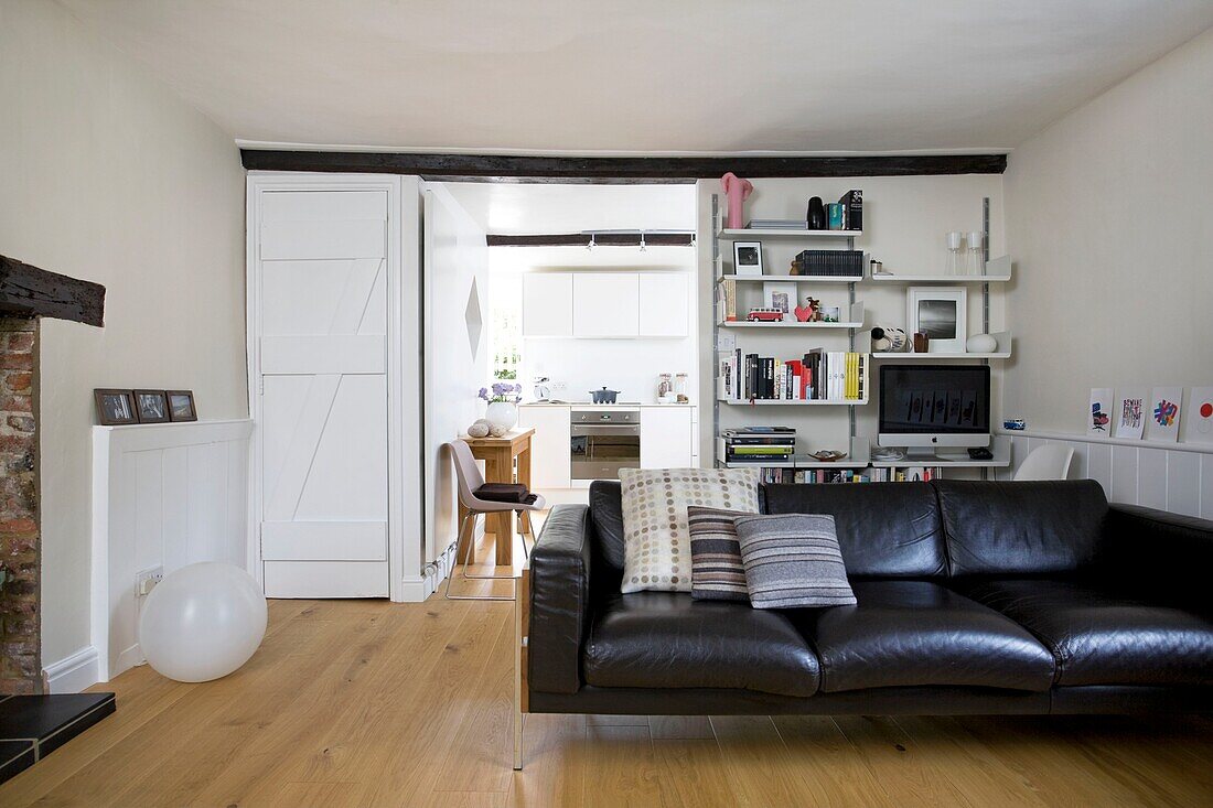 Brown leather sofa and storage shelves in white timber framed cottage