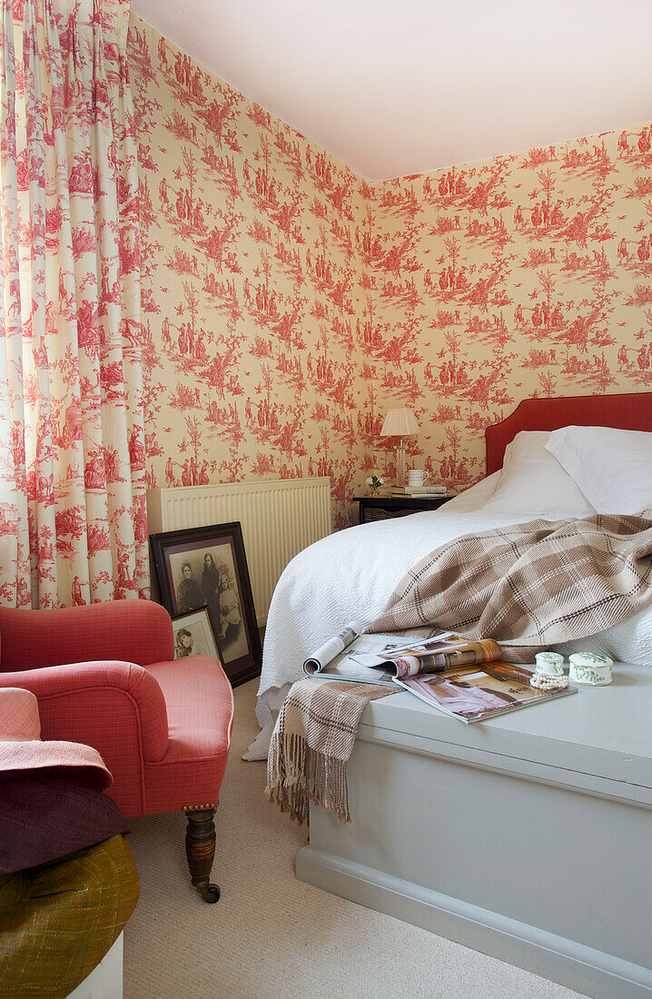 Roter Stuhl und gemusterte Tapete im Schlafzimmer eines Bauernhauses in Etchingham, East Sussex, England, UK