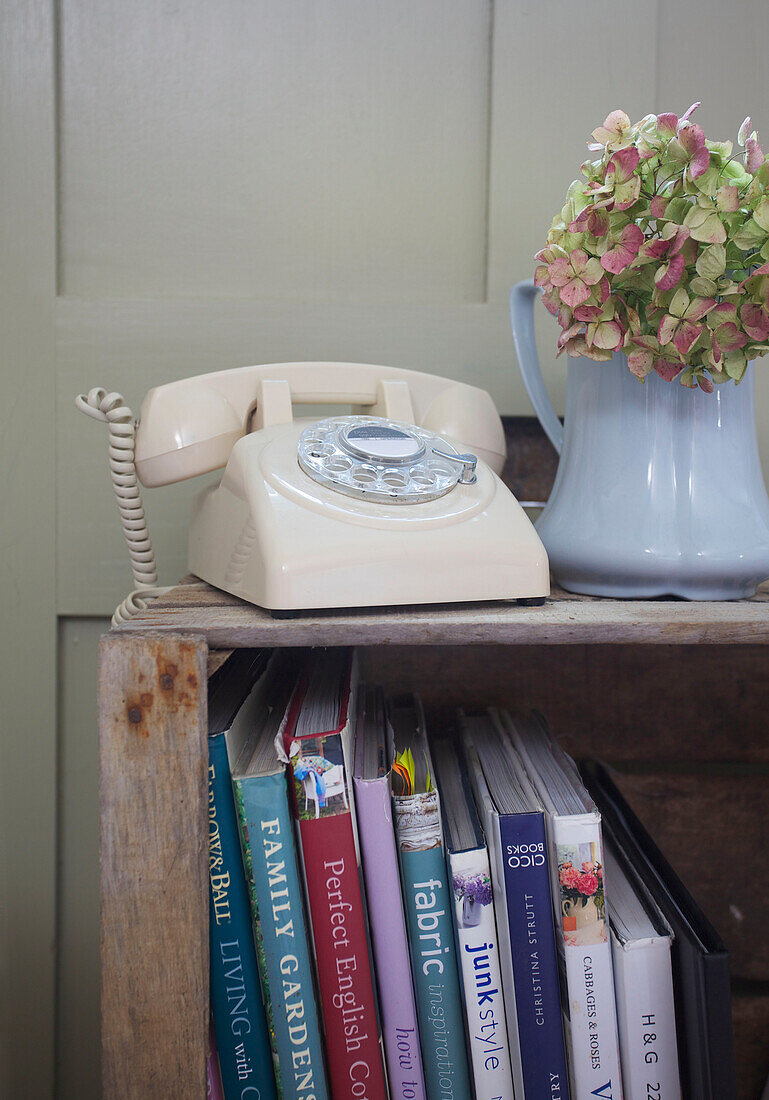Cream rotary dial telephone with hydrangea on wooden bookcase in High Halden farmhouse Kent England UK