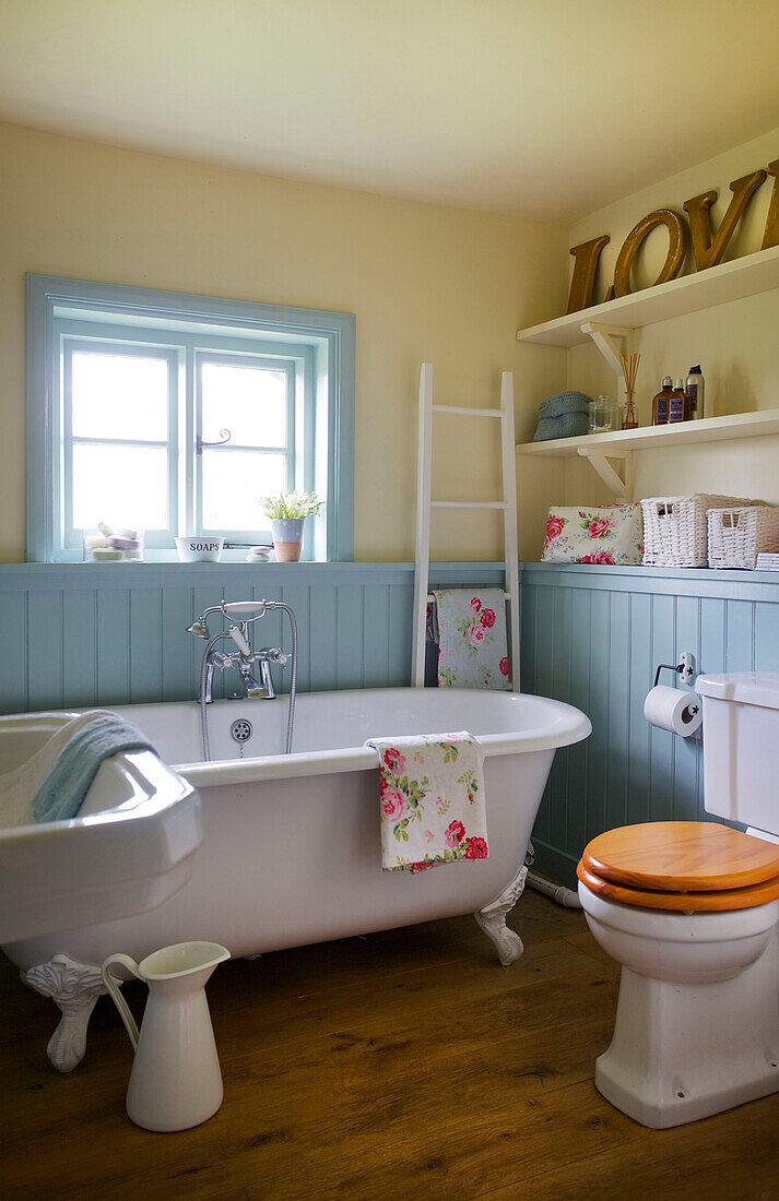 White ceramic freestanding bath in blue panelled bathroom in High Halden farmhouse Kent England UK