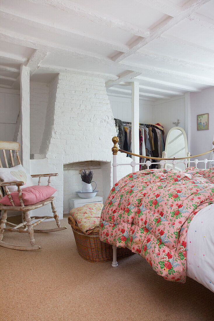 Geblümte Steppdecke auf einem Doppelbett mit Schaukelstuhl und weiß getünchtem Kamin in einem Bauernhaus in High Halden, Kent, England