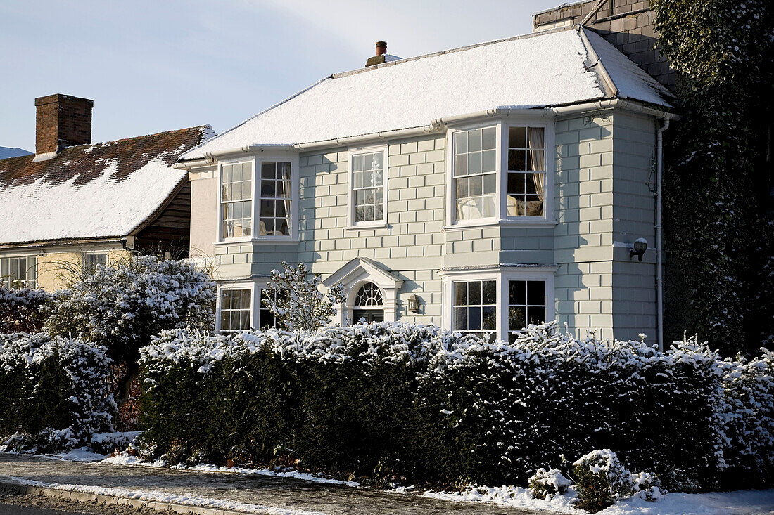 Painted home exterior with snowfall on hedge in Tenterden, Kent, England, UK