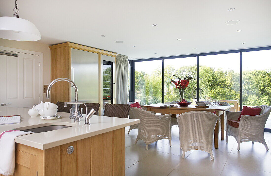 Open plan kitchen and dining room with cane furniture in contemporary farmhouse, Nuthurst, West Sussex, England, UK