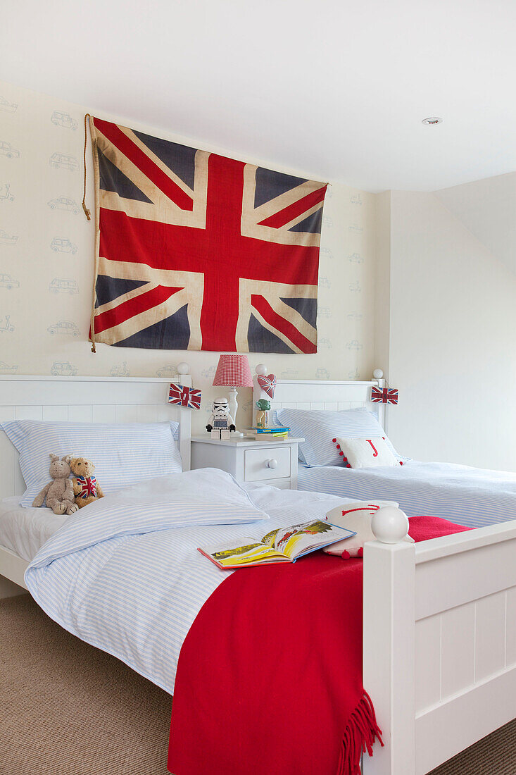 Union Jack hangs above twin beds with blue striped duvets and red blanket in Kilndown home Cranbrook Kent England UK