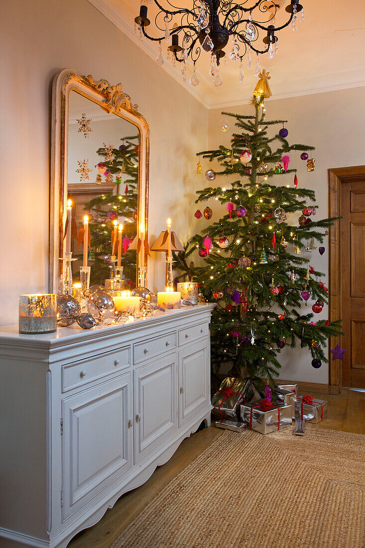 Lit candles on white sideboard with Christmas tree in hallway of Faversham home Kent England UK