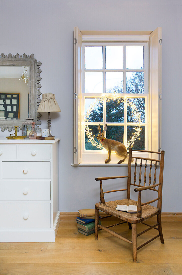 Wicker chair and lit lights with hare ornament at window of Faversham home Kent England UK