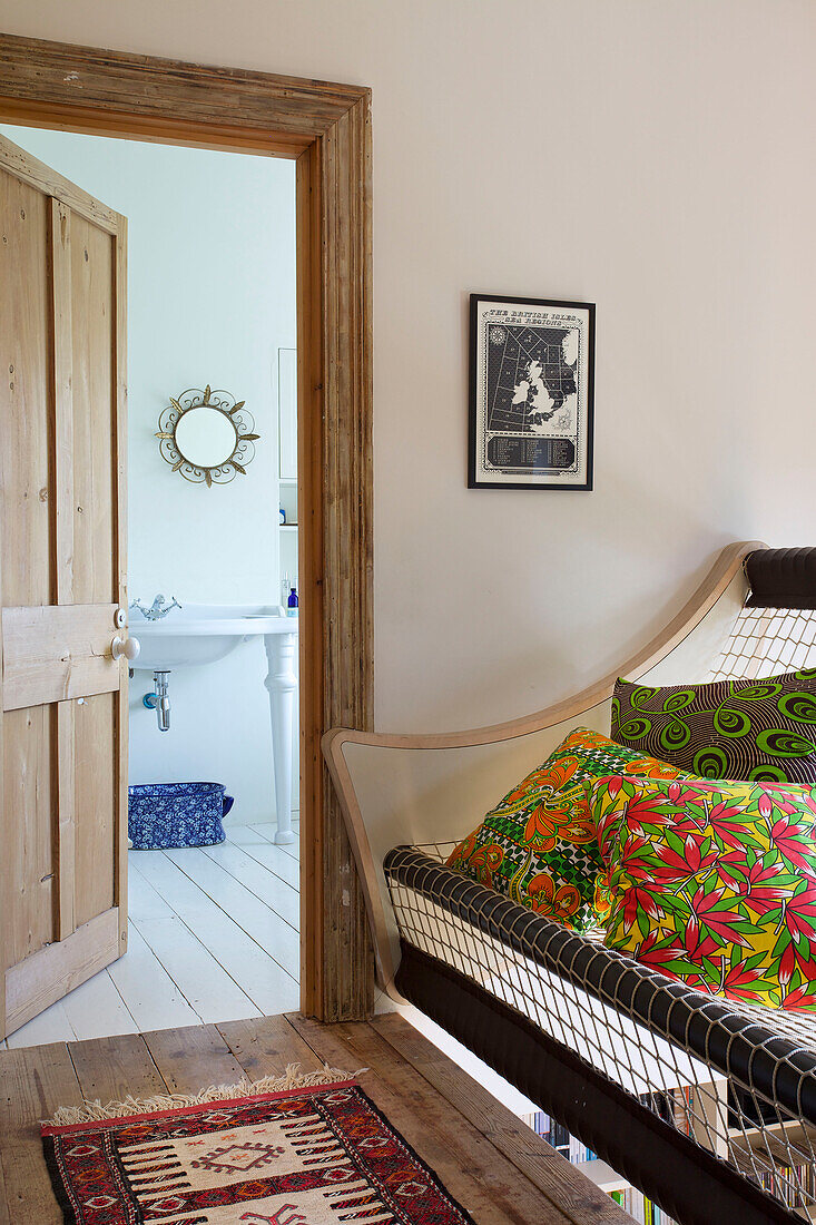 Floral print cushions on landing sofa with view through wooden doorframe in Hackney home London England UK