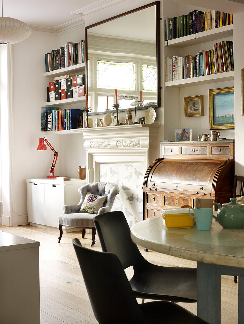 Large rectangular mirror above fireplace with bookshelves in open plan living and dining room of London home England UK