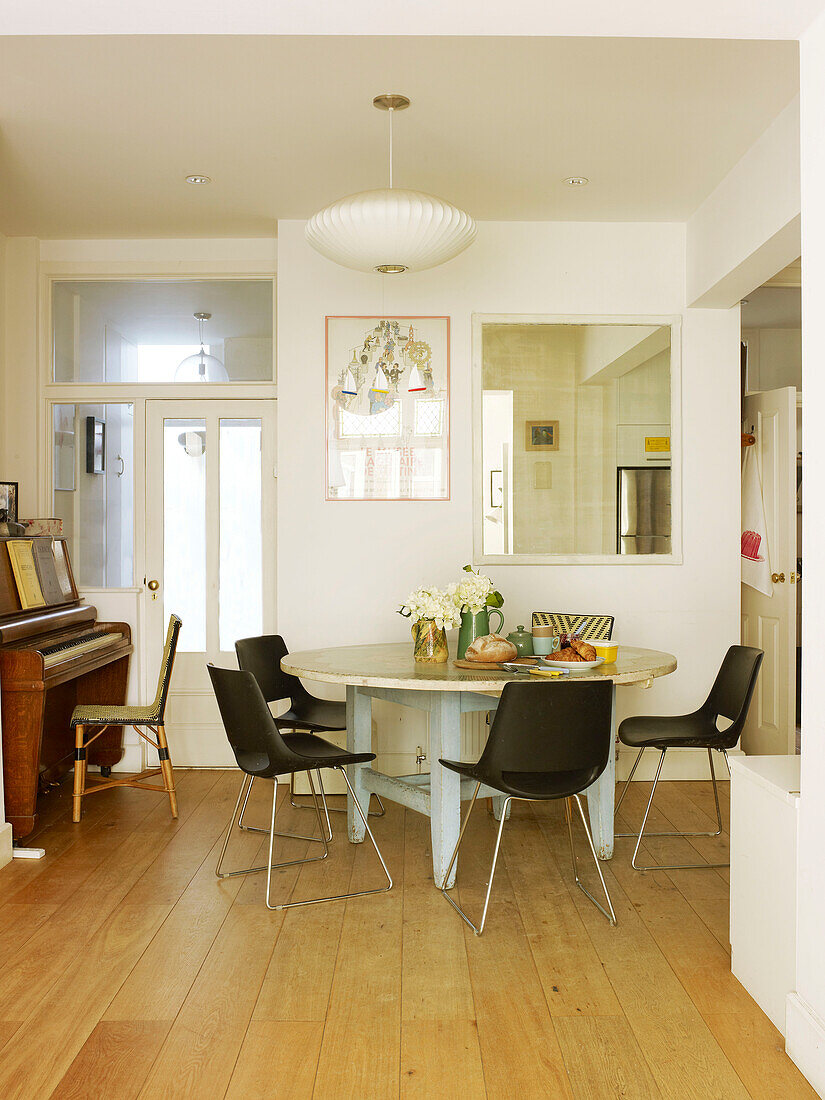 Black chairs at circular table with piano and mirror in London home England UK