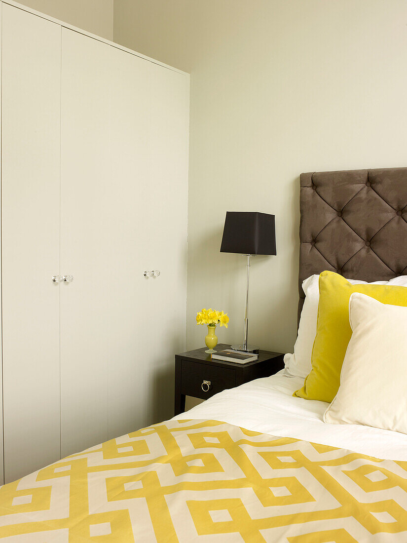 Black lamp on side table with geometric bed cover and buttoned headboard in Little Venice townhouse London England UK