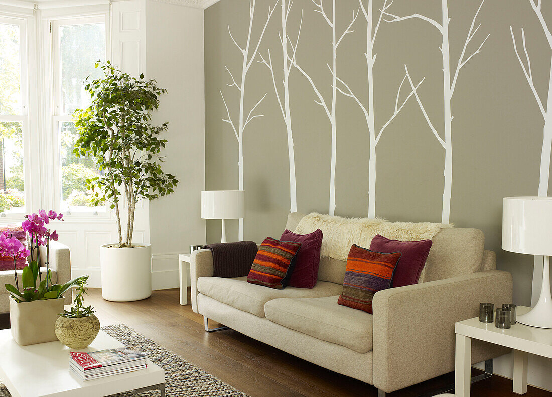 Striped cushions on cream sofa with tree wall deco in living room of London home, UK