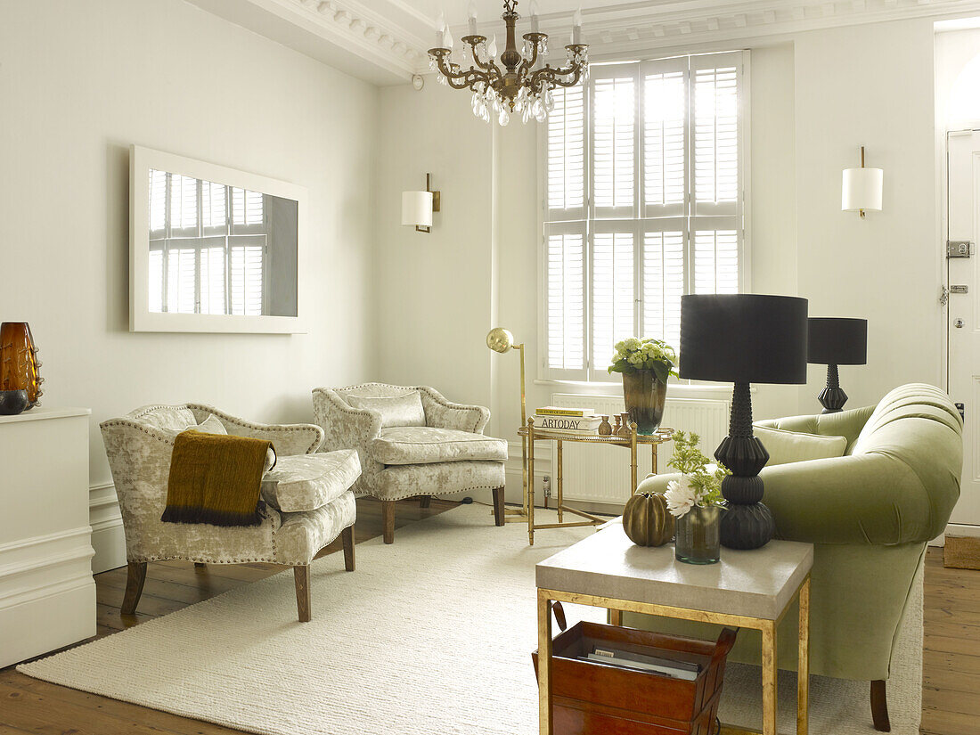 Black matching lamps with velvet armchairs and sofa in shuttered living room of North London townhouse England UK