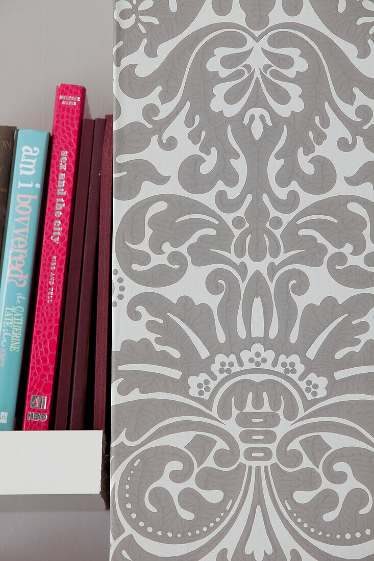 Books on shelf with grey patterned wallpaper in contemporary London home, England, UK