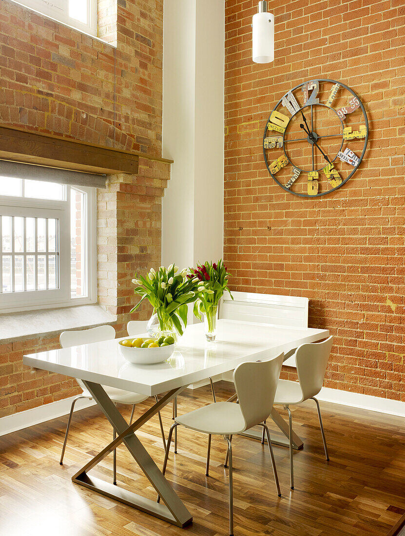 Metal clock above table with tulips at window of Ipswich warehouse conversion, Suffolk, England, UK