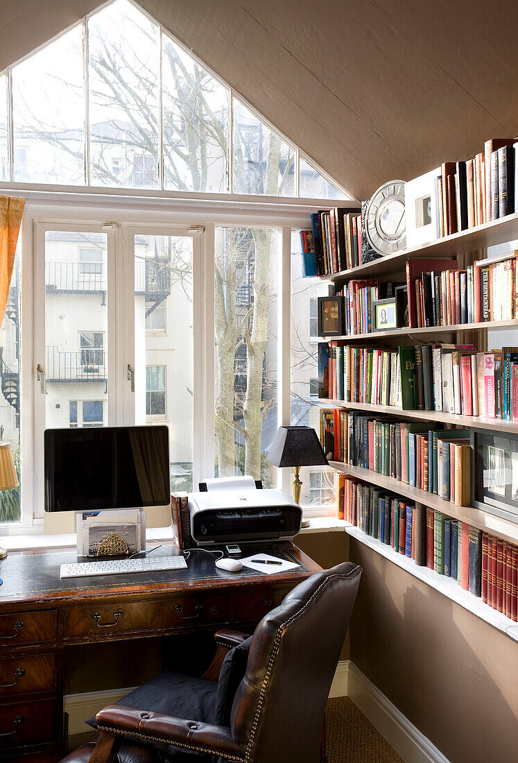 Desk with computer and chair at window with bookcase in Hove home East Sussex UK