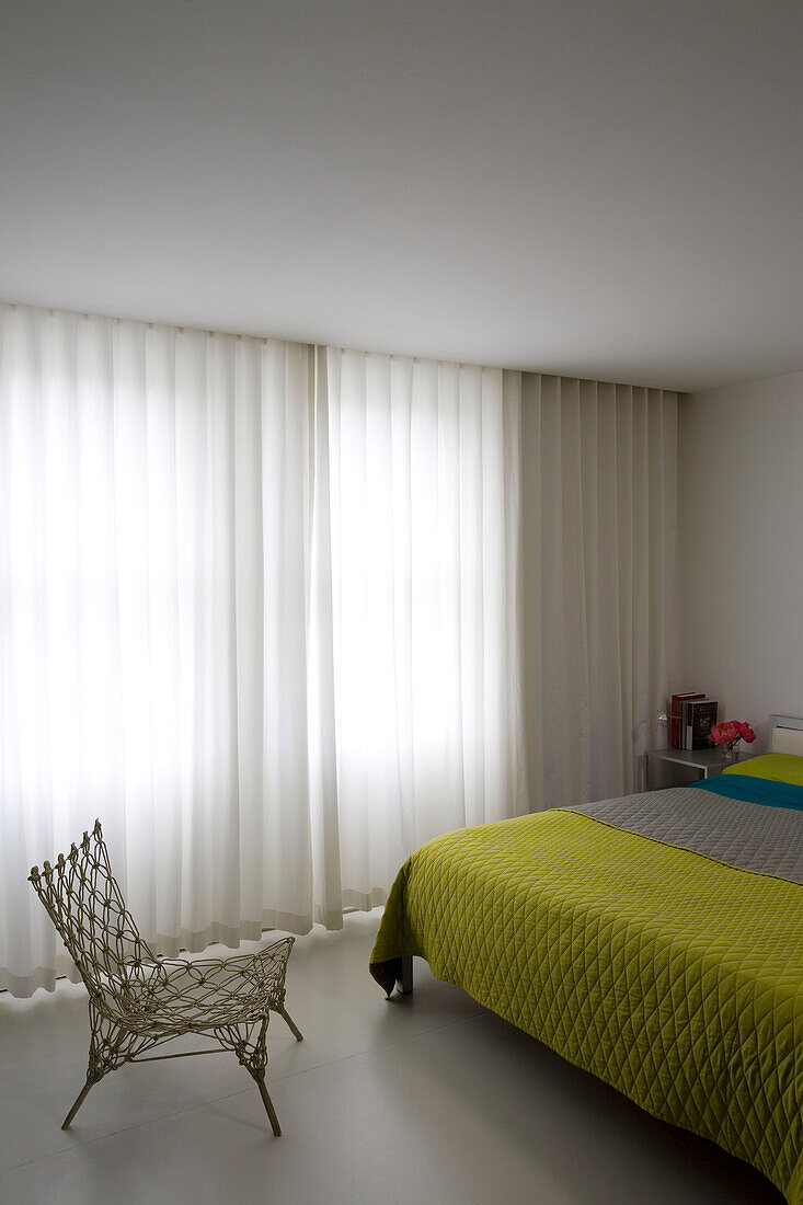 Low chair and yellow quilted cover with net curtains in bedroom of contemporary London apartment, England, UK